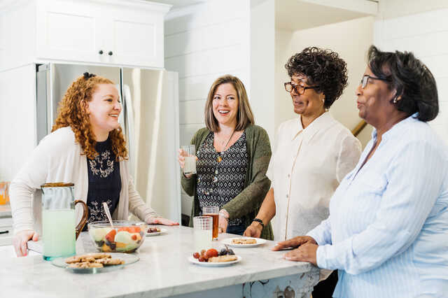 women standing around a kitchen island laughing and eating snacks